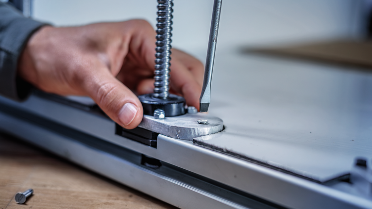 Person uses a screwdriver to adjust a metal fixture on a flat surface.