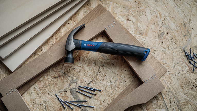 Hammer placed on wooden boards with scattered nails on a plywood surface.