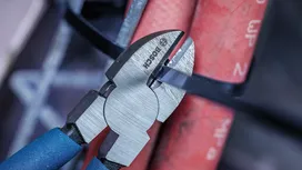 Wire cutter snips a black cable tie around red pipes.