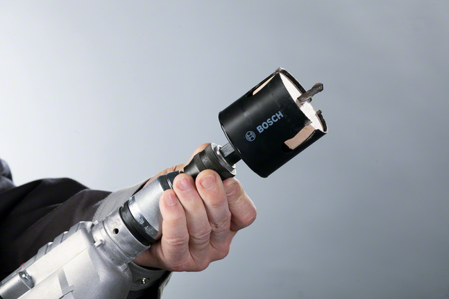 Hand holding a power drill fitted with a hole saw bit.