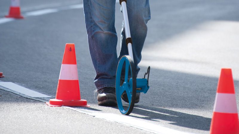 Une personne utilise une roue de mesure pour vérifier la distance sur la route à côté des cônes de signalisation orange.