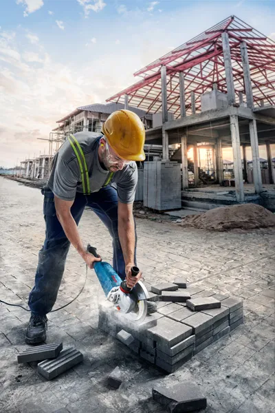 Une personne portant un équipement de sécurité coupe des pavés avec une découpeuse électrique sur un chantier de construction.