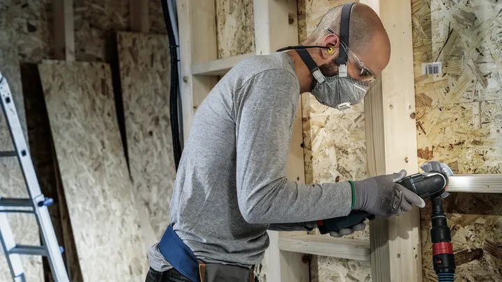 Une personne portant un équipement de sécurité perce un cadre en bois.