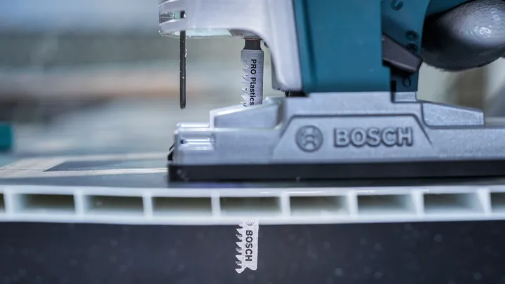 Une scie sauteuse coupe un épais panneau en plastique dans une scène d'atelier en gros plan.