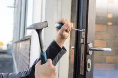 Une personne utilise un tournevis et un marteau pour régler une serrure de porte.