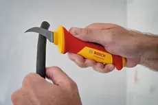 Une personne utilise un couteau isolé pour dénuder un câble noir.