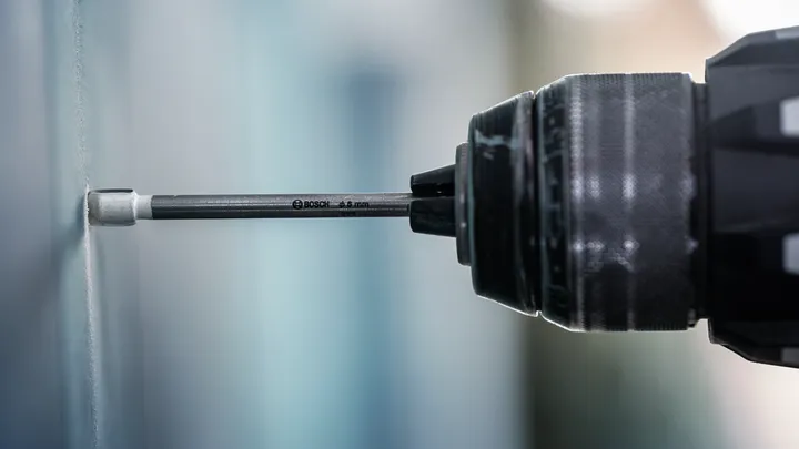 Perceuse enfonçant une vis dans un mur.