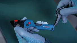 Une personne portant un équipement de sécurité tient un couteau utilitaire bleu et en change la lame.