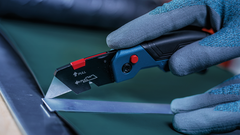 Une personne portant un équipement de sécurité utilise un cutter pour découper une feuille de matériau.