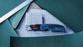 Un couteau utilitaire posé sur un tissu à quadrillage entouré de panneaux verts.
