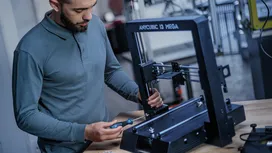Une personne assemble une imprimante 3D à l'aide d'un tournevis sur un établi.