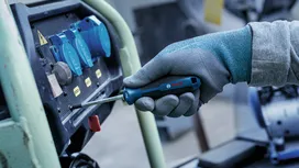 Une personne portant un équipement de sécurité serre une vis sur un panneau de commande industriel.