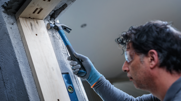 Une personne portant un équipement de sécurité utilise un marteau pour travailler sur un mur en béton.