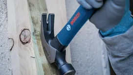 Une personne portant un équipement de sécurité utilise un marteau pour fixer une planche de bois à un mur.