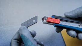 Une personne portant un équipement de sécurité remplace la lame d'un couteau utilitaire.