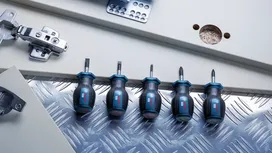 Cinq tournevis trapus alignés sur une surface métallique près des ferrures d'un meuble.