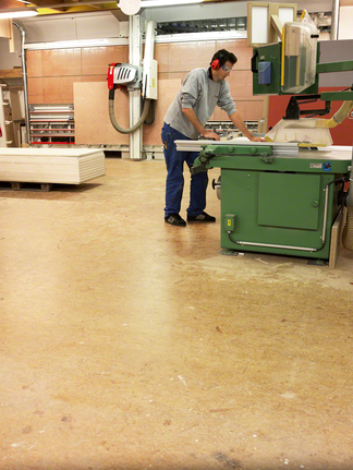 Ouvrier utilisant une scie circulaire dans un atelier, portant un équipement de sécurité.