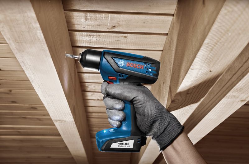 Una persona que usa equipo de seguridad perfora una viga de madera del techo usando un taladro inalámbrico.