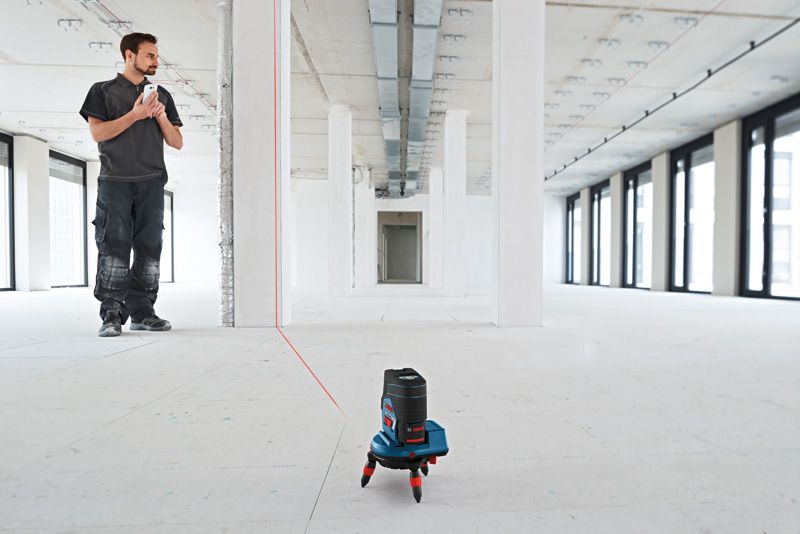 Persona utilizando un nivel láser para proyectar líneas rectas en una habitación sin terminar.