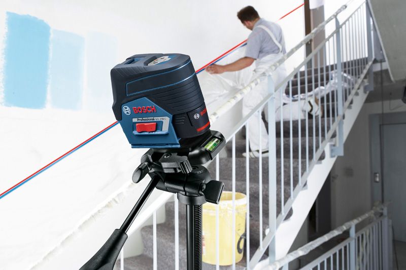 Herramienta de nivelación láser que proyecta líneas a través de una escalera mientras una persona prepara una pared.