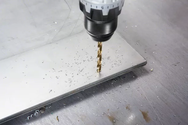 Taladro inalámbrico haciendo un agujero en una chapa metálica, virutas de metal esparcidas por todas partes.