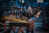 Una persona que usa equipo de seguridad muele metal, creando chispas en un taller industrial.