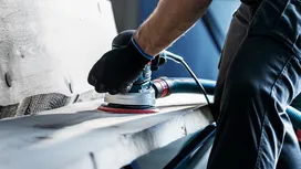 Una persona que usa equipo de seguridad utiliza una lijadora para alisar una tabla de madera.