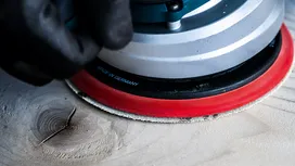 Una persona que usa equipo de seguridad lija una superficie de madera con una lijadora eléctrica.