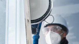 Una persona que usa equipo de seguridad utiliza una herramienta eléctrica para cortar una superficie de madera.