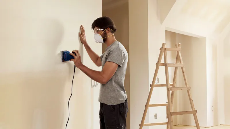 Hombre lijando pared en interior.