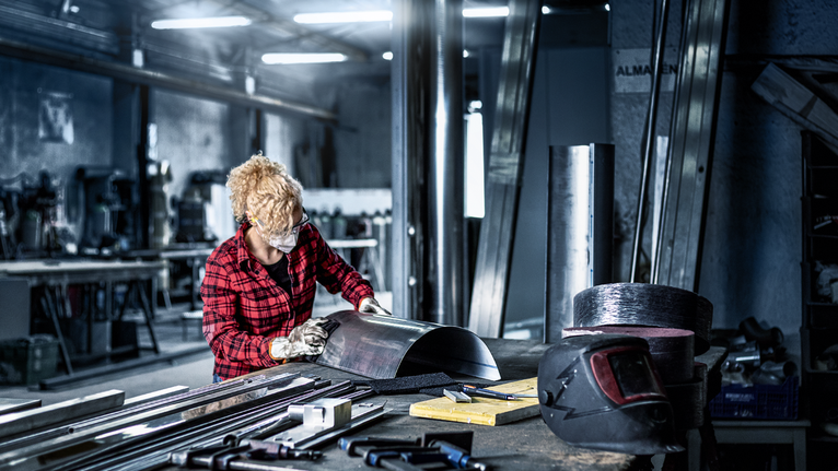 Persona que usa equipo de seguridad dando forma a una lámina de metal en un taller.