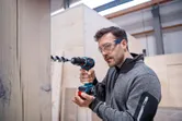 Una persona que usa equipo de seguridad perfora madera utilizando un taladro atornillador inalámbrico.