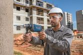 Una persona que usa equipo de seguridad perfora una pared de hormigón en un sitio de construcción.