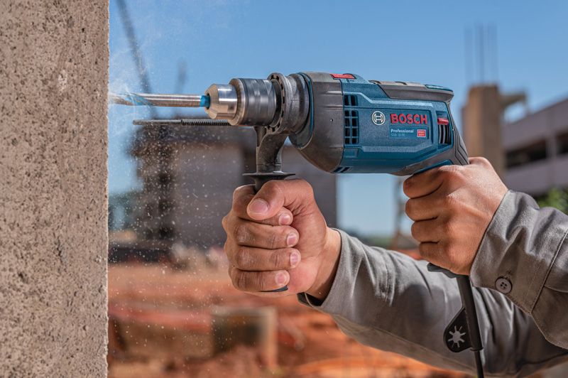 Una persona que usa equipo de seguridad perfora hormigón con un taladro de impacto.