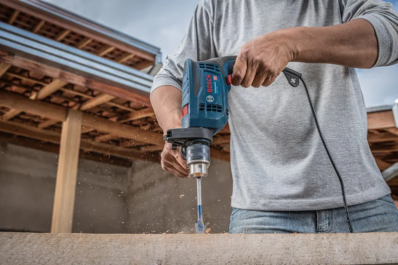 Una persona perfora madera con un taladro de impacto en un entorno de construcción.
