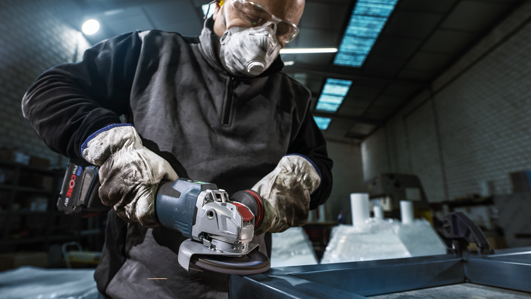 Una persona que usa equipo de seguridad muele metal utilizando una amoladora angular inalámbrica.