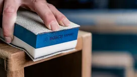 Persona lijando el borde de un mueble de madera con un bloque de lijado rectangular.