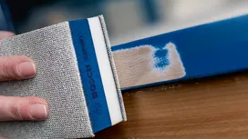 Persona lijando una superficie de madera pintada de azul.