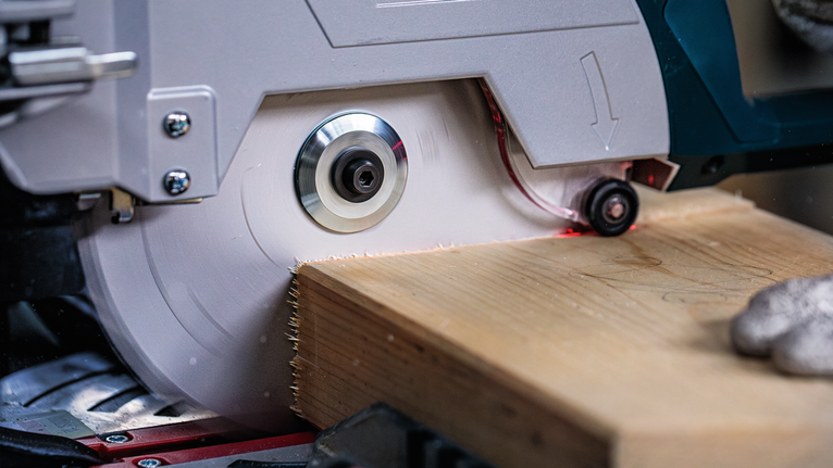 Una persona que usa equipo de seguridad corta una tabla de madera con una sierra circular.