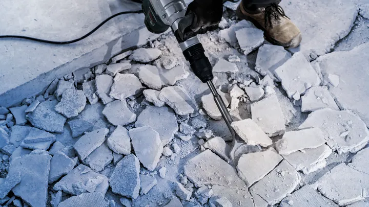 Persona con equipo de seguridad rompiendo un piso de concreto con un martillo demoledor.