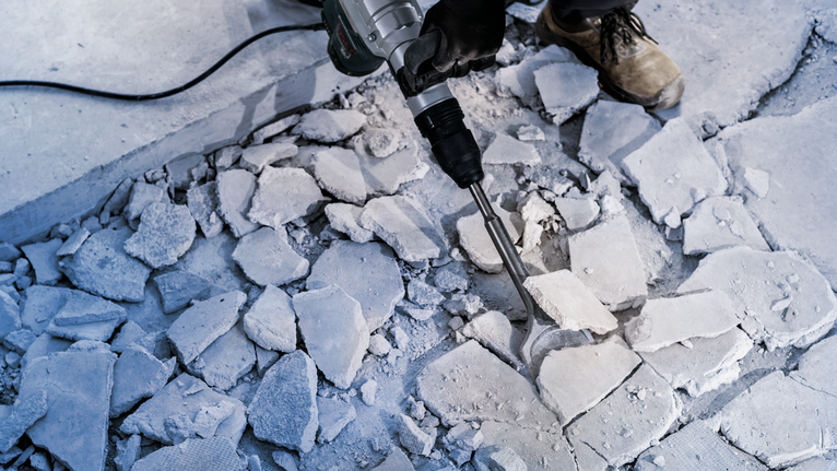Persona con equipo de seguridad rompiendo un piso de concreto con un martillo demoledor.