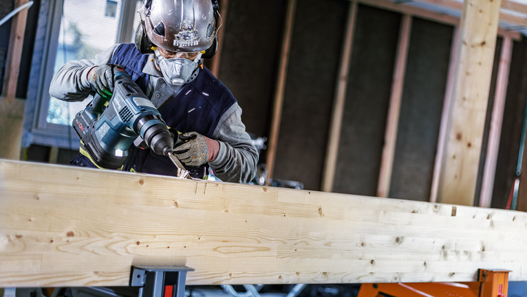 Una persona que usa equipo de seguridad perfora una viga de madera en un sitio de construcción.