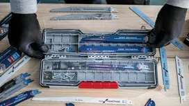 Una persona que lleva puesto un equipo de seguridad organiza hojas de sierra y tornillos de diferentes tipos en una caja de plástico.