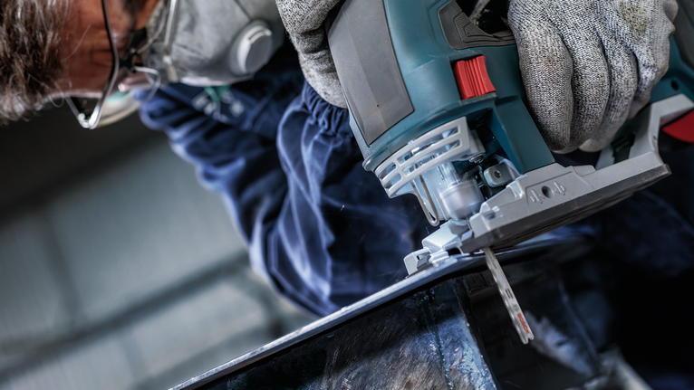 Una persona que usa equipo de seguridad utiliza una sierra caladora para cortar metal.