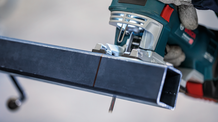Una persona que usa equipo de seguridad utiliza una sierra caladora para cortar una viga de metal.