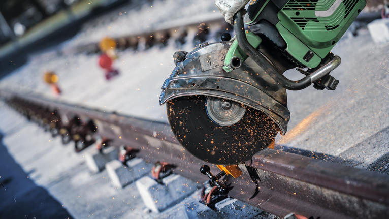 Sierra de corte generando chispas mientras corta una vía férrea al aire libre.