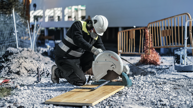Una persona que usa equipo de seguridad corta una tabla de madera con una sierra circular en un sitio de construcción.