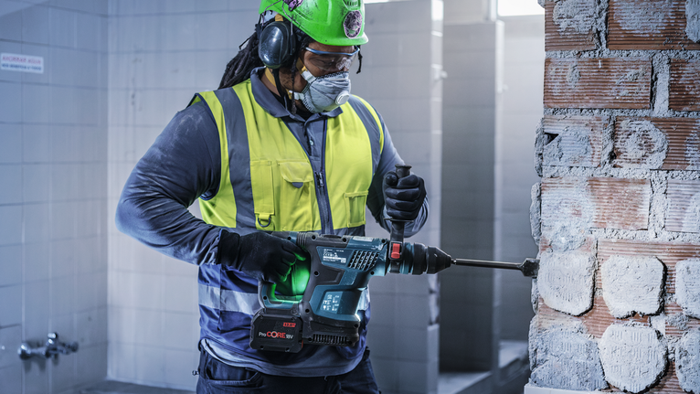 Un trabajador que usa equipo de seguridad perfora una pared de ladrillos con una herramienta eléctrica.