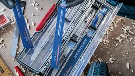 Una persona que lleva puesto el equipo de seguridad selecciona una hoja de sierra de una caja de herramientas organizada.
