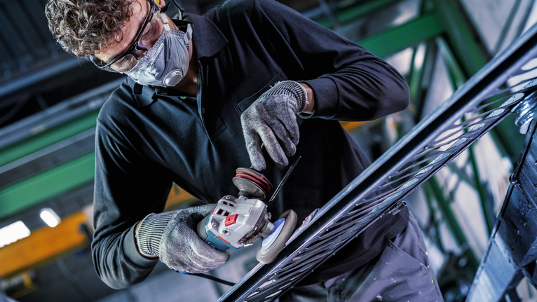 Una persona que usa equipo de seguridad muele metal en un marco grande en un taller industrial.